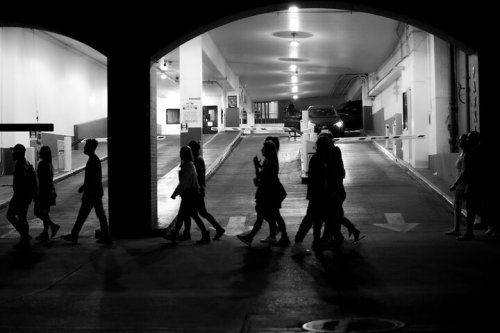 Silhouettes of people walking through a dimly lit parking garage entrance at night.