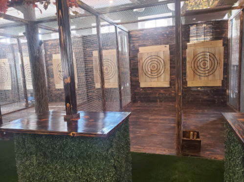 Indoor axe-throwing venue with wooden targets, surrounded by a mesh enclosure and a grassy floor.