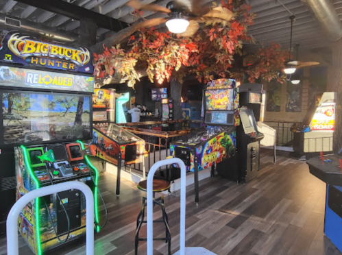 A vibrant arcade with various games, including pinball machines and a Big Buck Hunter game, surrounded by autumn-themed decor.
