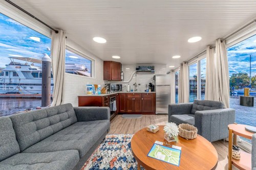 Cozy interior of a modern houseboat with a kitchen, seating area, and large windows overlooking the water.