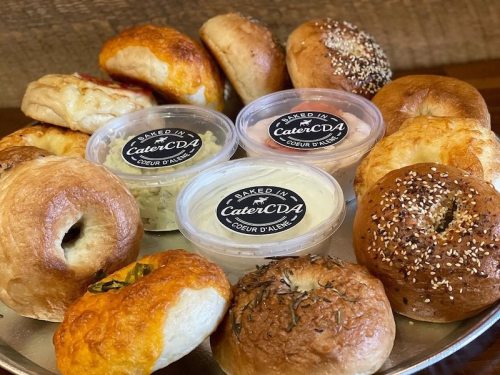 A platter of assorted baked goods, including bagels and rolls, with two containers of cream cheese.