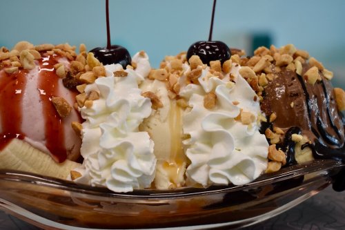 A delicious ice cream sundae with three scoops, topped with whipped cream, nuts, chocolate, and cherry.