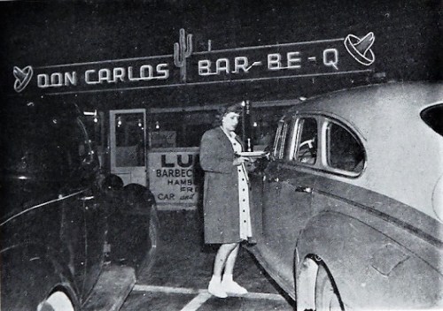 A woman stands by a car at night in front of Don Carlos Bar-Be-Q, with neon signs and cacti in the background.