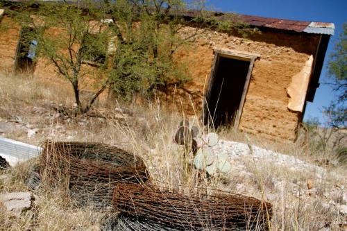 Abandoned building with a weathered exterior, surrounded by dry grass, barbed wire, and a cactus.