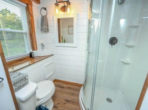 Bright bathroom featuring a shower, toilet, sink, and wooden accents with natural light from a window.