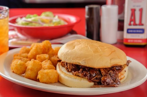A plate featuring a pulled beef sandwich, crispy tater tots, and a side salad in a vibrant diner setting.