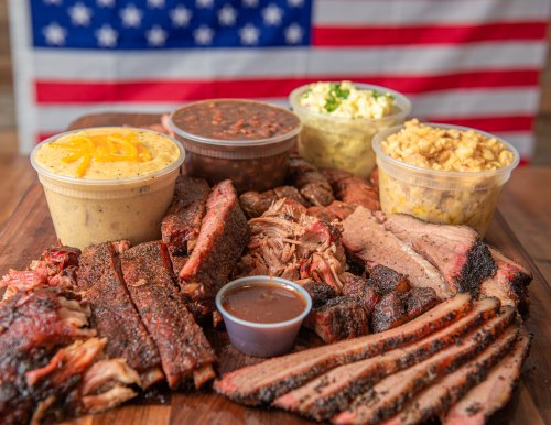 A platter of assorted barbecue meats with sides, set against a backdrop of an American flag.
