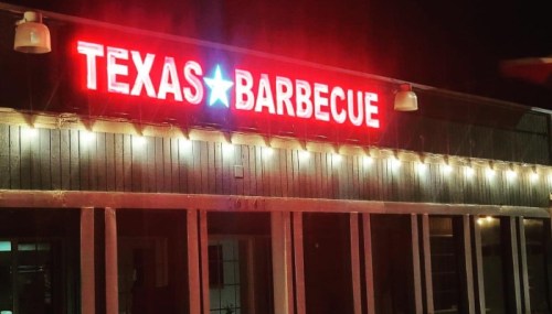 Neon sign reading "Texas Barbecue" illuminated at night on a restaurant exterior.