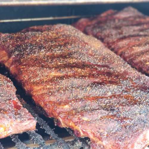 Close-up of perfectly smoked ribs with a rich, dark crust, resting on a grill.
