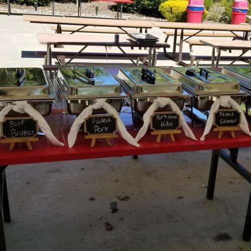 A table with chafing dishes labeled for beef brisket, pulled pork, pork spare ribs, and Texas caviar.