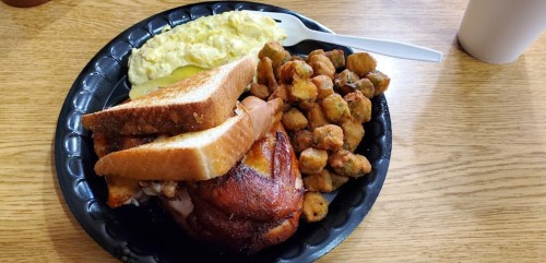 A plate with grilled chicken, scrambled eggs, fried okra, and two slices of toast on a wooden table.