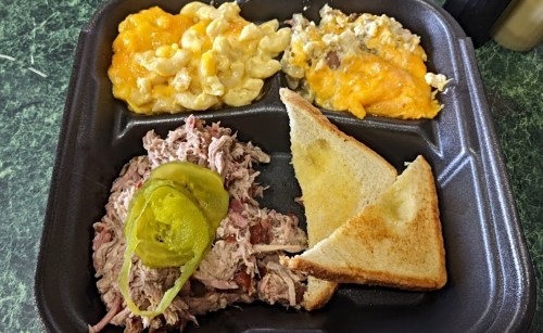 A divided food tray with pulled pork topped with jalapeños, macaroni and cheese, and a cheesy casserole, plus two slices of toast.