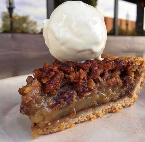 A slice of pecan pie topped with a scoop of vanilla ice cream on a white plate.