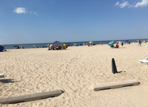 A sunny beach scene with colorful umbrellas, people relaxing, and a clear blue sky.