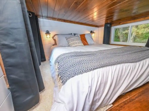 Cozy bedroom with a wooden ceiling, a large bed, and soft lighting, surrounded by dark curtains and a plush rug.