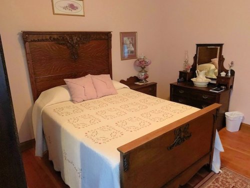 A cozy bedroom featuring a wooden bed, decorative pillows, a dresser, and vintage decor in soft colors.
