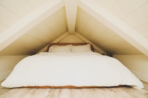 Cozy attic bedroom with a sloped ceiling, featuring a large bed covered in white bedding.