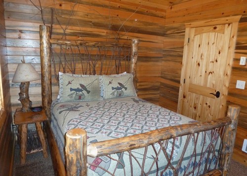 Cozy log cabin bedroom with a wooden bed, patterned bedding, and rustic decor against a wood-paneled wall.