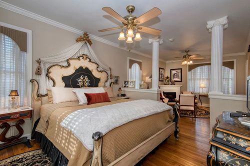 Elegant bedroom featuring a large ornate bed, decorative ceiling fan, and classic furnishings with warm lighting.