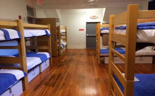 A dormitory room with wooden bunk beds, blue bedding, and polished wooden floors.