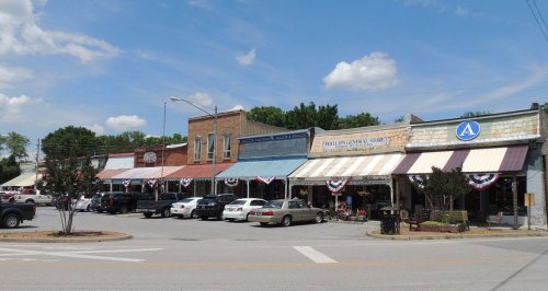 A charming small-town street with historic buildings, shops, and festive bunting on a sunny day.
