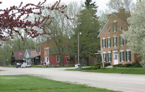 A quiet rural street lined with historic brick buildings, trees, and a stop sign, showcasing a peaceful small-town atmosphere.