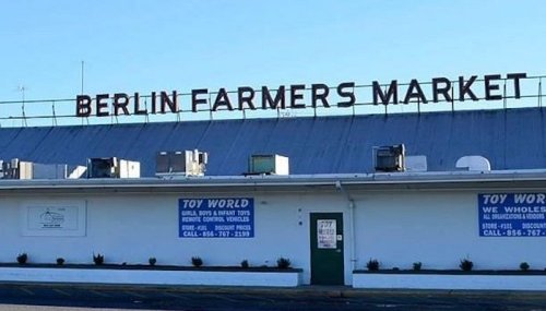 Sign for Berlin Farmers Market with a Toy World advertisement on the building's exterior. Clear blue sky above.