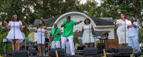 A lively music performance featuring a group of singers and musicians on stage, all dressed in white and green.