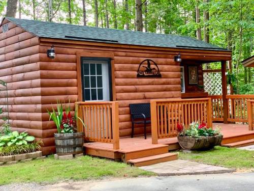 A cozy log cabin with a wooden deck, surrounded by greenery and colorful flowers.
