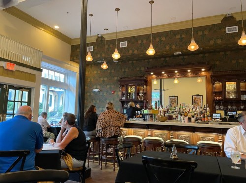 A stylish bar area in a restaurant with patrons seated at tables and a bartender preparing drinks.