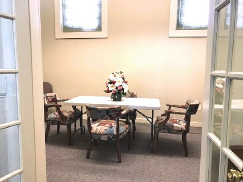 A small room with a table and four chairs, decorated with a floral centerpiece and soft lighting.