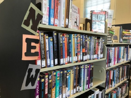 Bookshelves filled with various books, featuring a sign that says "NEW" in colorful letters.