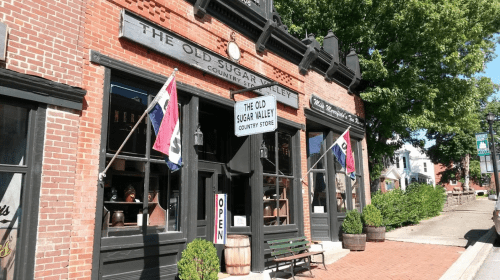 A charming brick storefront with flags, featuring "The Old Sugar Valley Country Store" sign and an open sign.