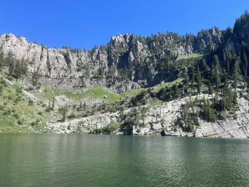 A serene lake surrounded by steep cliffs and lush greenery under a clear blue sky.