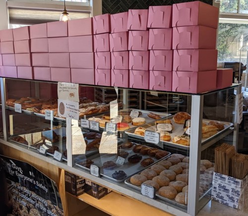A display case filled with various pastries and donuts, topped with stacks of pink boxes.