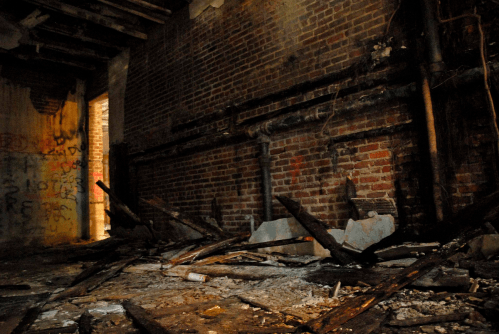 A dimly lit, abandoned room with exposed brick walls, debris, and graffiti on the walls.