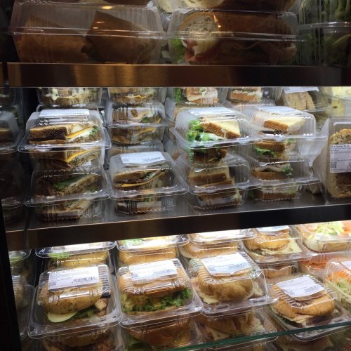 A display case filled with various sandwiches in clear plastic containers, stacked neatly on shelves.