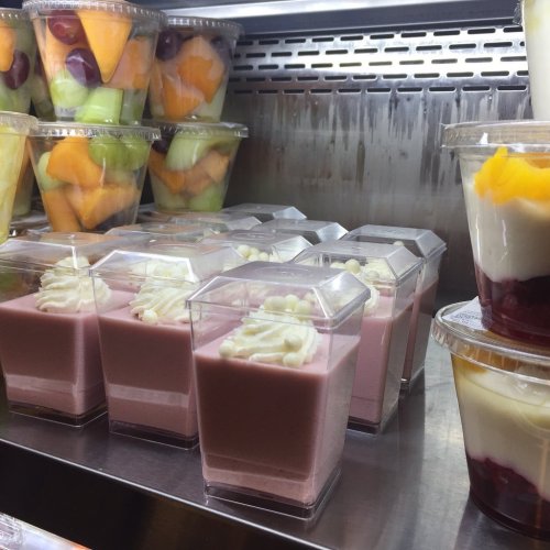 A display of dessert cups with pink mousse topped with cream, alongside containers of assorted fresh fruit.