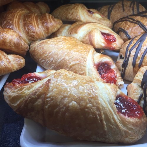 A display of freshly baked pastries, including croissants filled with red fruit jam and drizzled chocolate treats.
