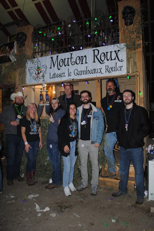 A group of people posing together at a festive event, with decorations and a sign reading "Mouton Roux."