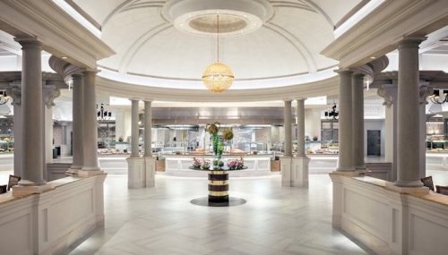 Elegant restaurant interior featuring a central chandelier, marble floors, and decorative columns. Bright and spacious ambiance.