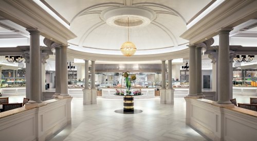 Elegant restaurant interior featuring a central floral display, high ceilings, and a buffet area in the background.