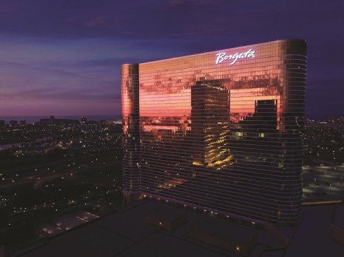 Aerial view of the Borgata Hotel, reflecting a colorful sunset in its glass facade, surrounded by city lights.