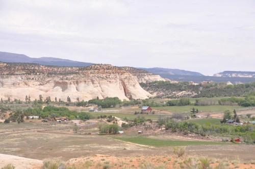A scenic view of rolling hills and cliffs, with a winding road and small farms in a lush green valley.