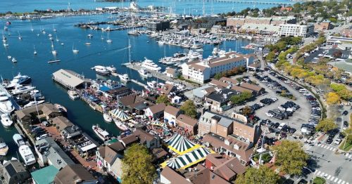 Aerial view of a bustling marina with boats, shops, and colorful tents along the waterfront.