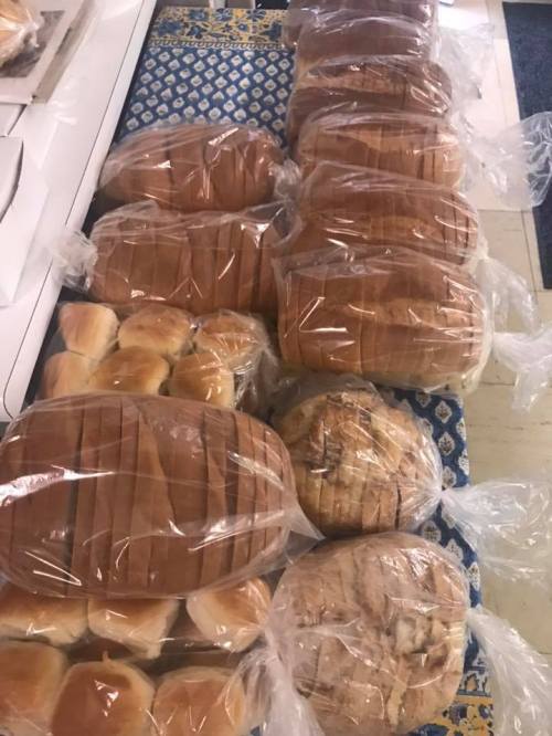 A variety of loaves and rolls of bread, all packaged in clear plastic bags, arranged on a table.