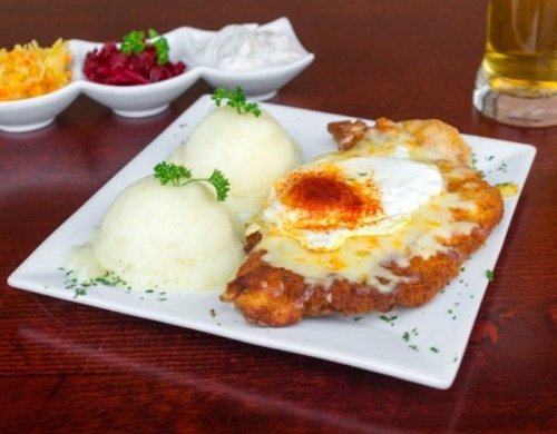 A plate of breaded chicken topped with cheese and an egg, served with mashed potatoes and side dishes.
