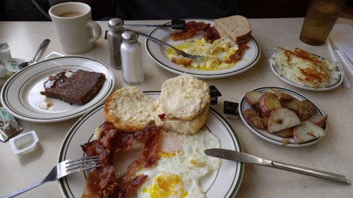 A breakfast spread featuring eggs, bacon, biscuits, hash browns, toast, and coffee on a table.