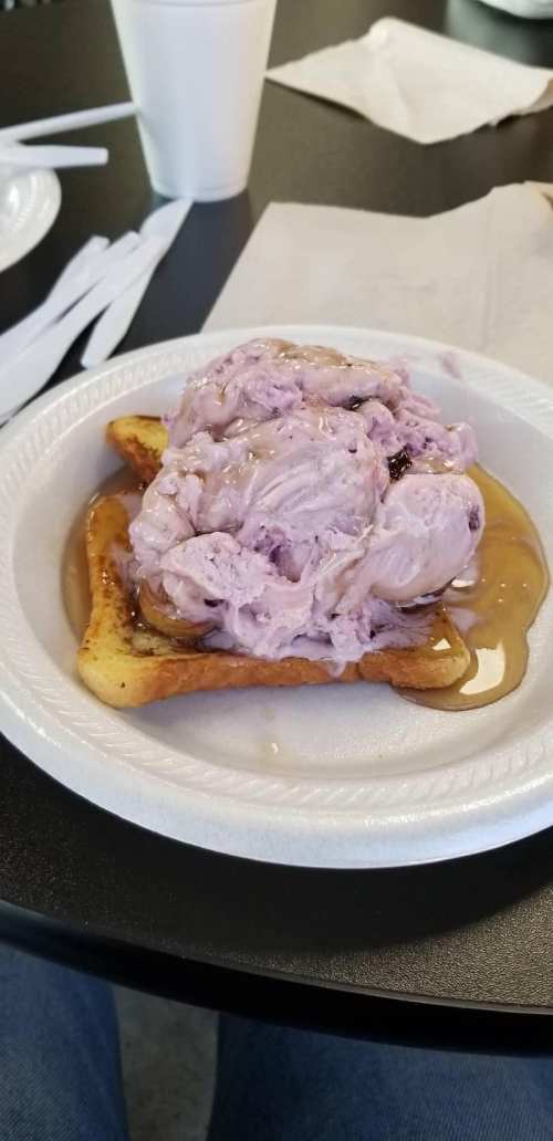 A plate with two pieces of toast topped with purple ice cream and drizzled with syrup.