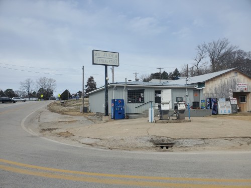 A small general store with gas pumps, located at a road intersection in a rural area.
